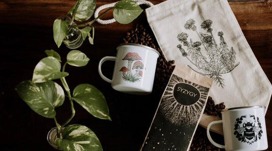 A flat lay of various Fennec Design products on a wooden table featuring mugs, coffee bag, lunch bag, and two pothos plants for decor