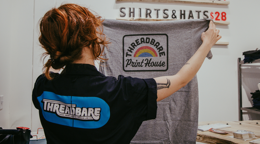 A person with red hair holds a grey Threadbare Press shirt