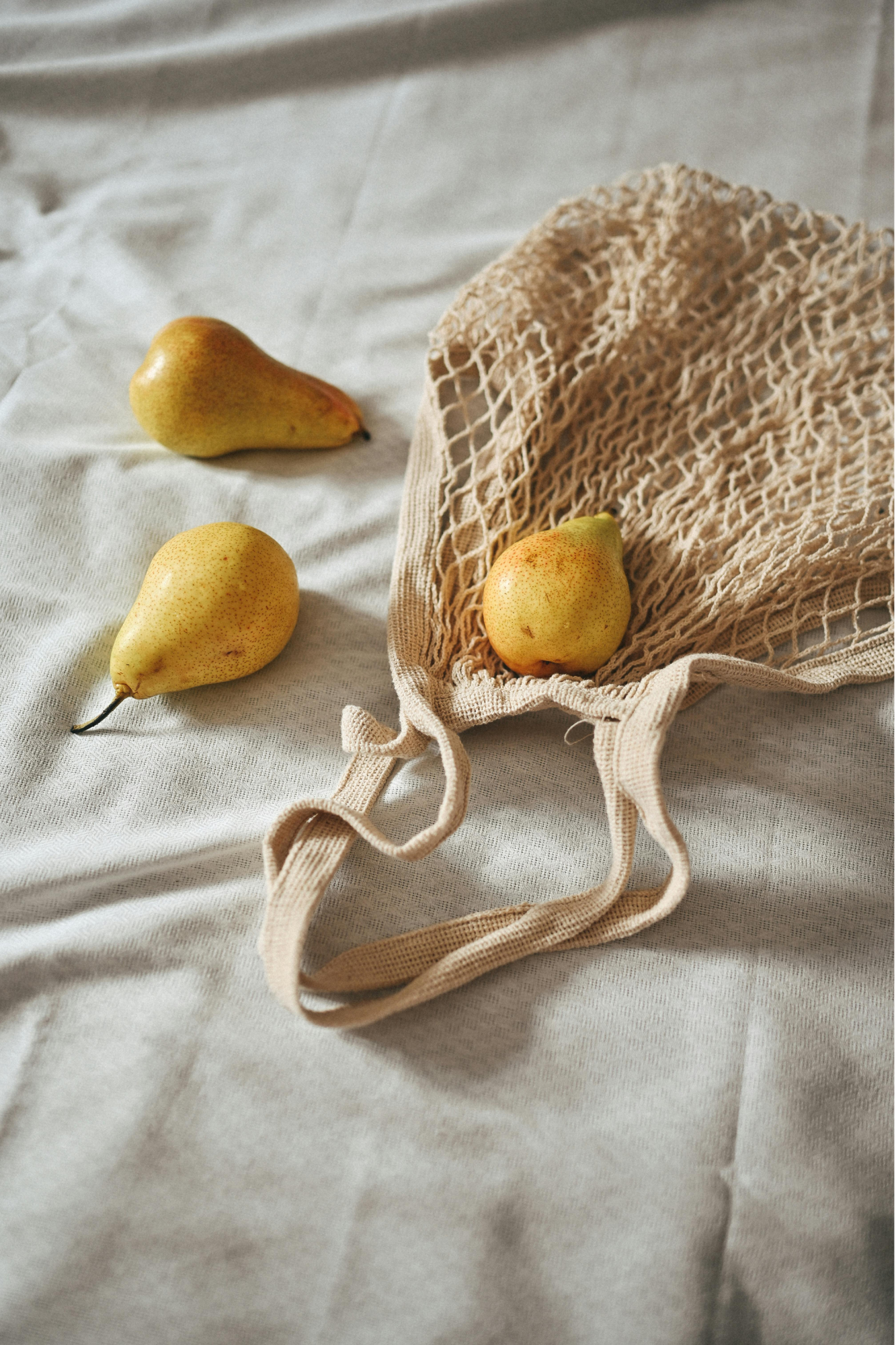 image of an undyed string bag on a textile with 3 pears on top